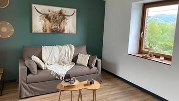 Una sala de estar con un sofá, dos mesitas auxiliares, una obra de arte enmarcada de un toro y un ventanal con vistas.