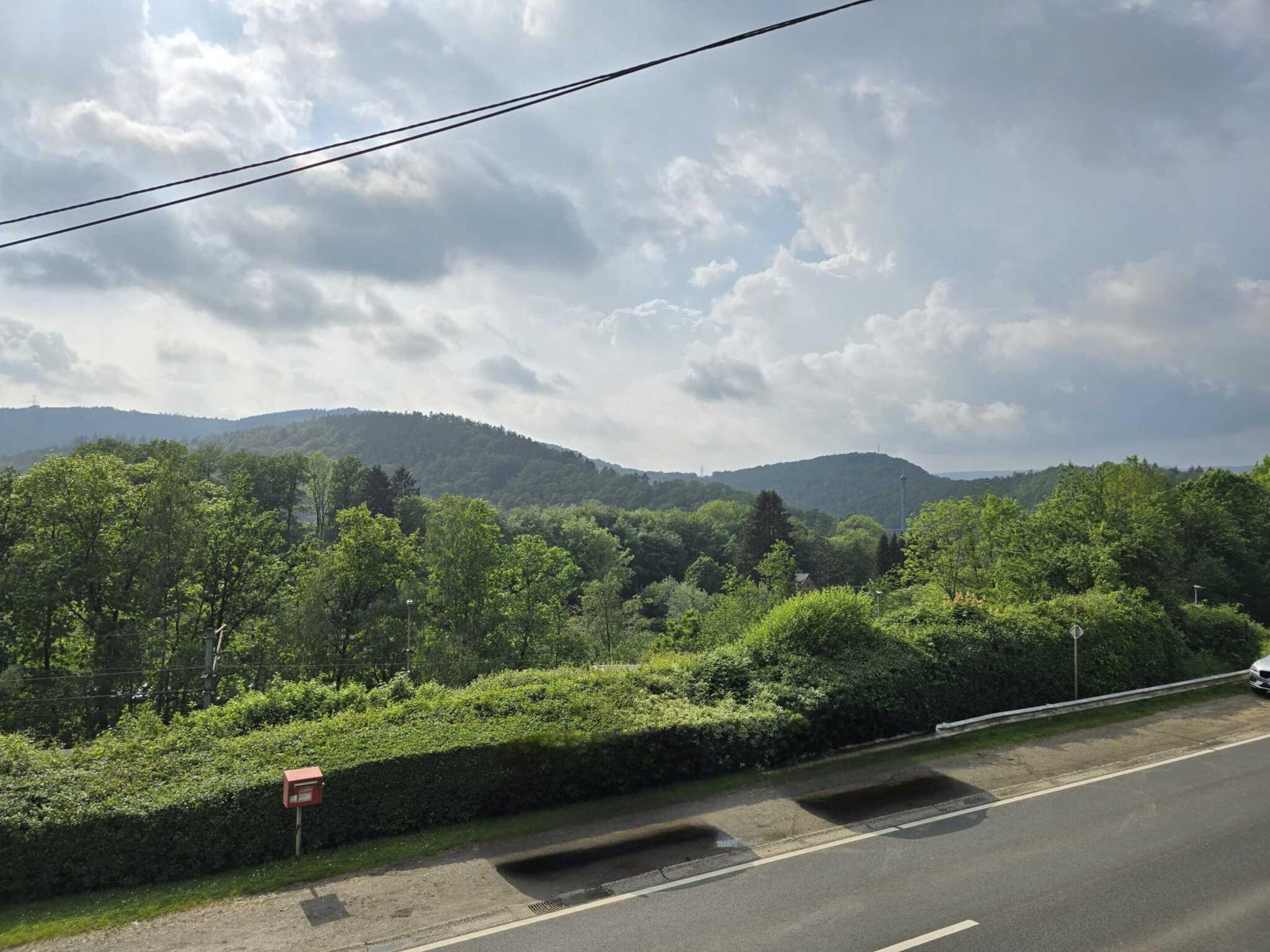 A road with a guardrail, surrounded by lush greenery and hills in the background.