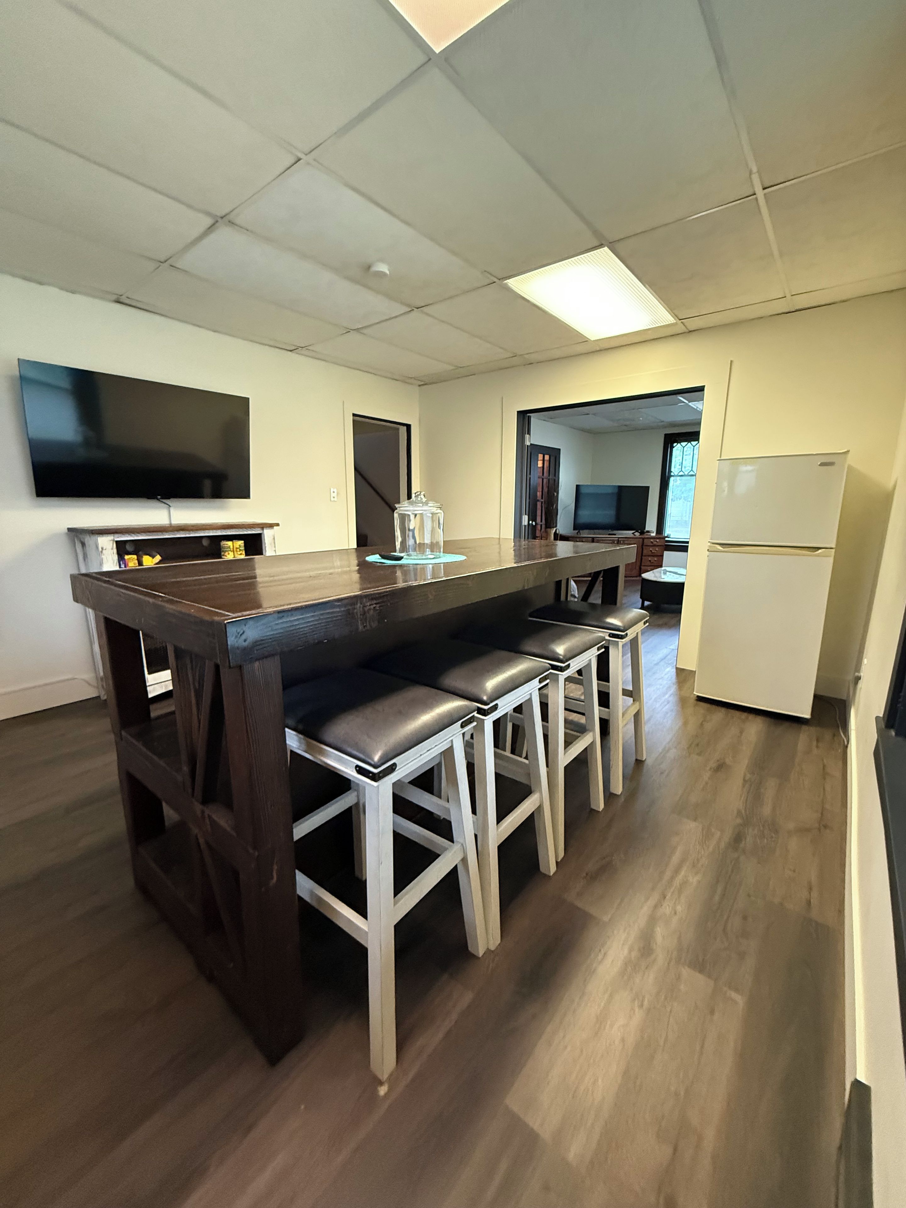 Una cocina moderna con una isla central, taburetes de bar, un televisor de pantalla plana y un refrigerador.