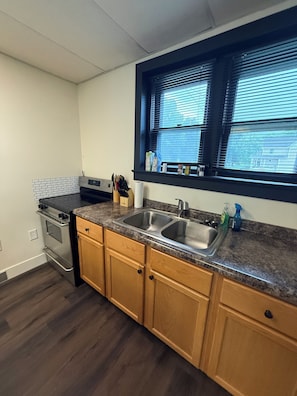A kitchen with a double sink, wooden cabinets, a stove, and a window with blinds. - "The Office" themed house in charming Topeka (Topeka)