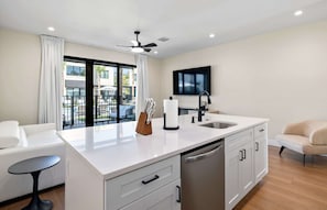 A modern kitchen with a central island, a built-in dishwasher, and a large window overlooking a pool area. - Cassa Orlando: Luxury Poolside 3BR/3BA Unit 109 (Orlando)