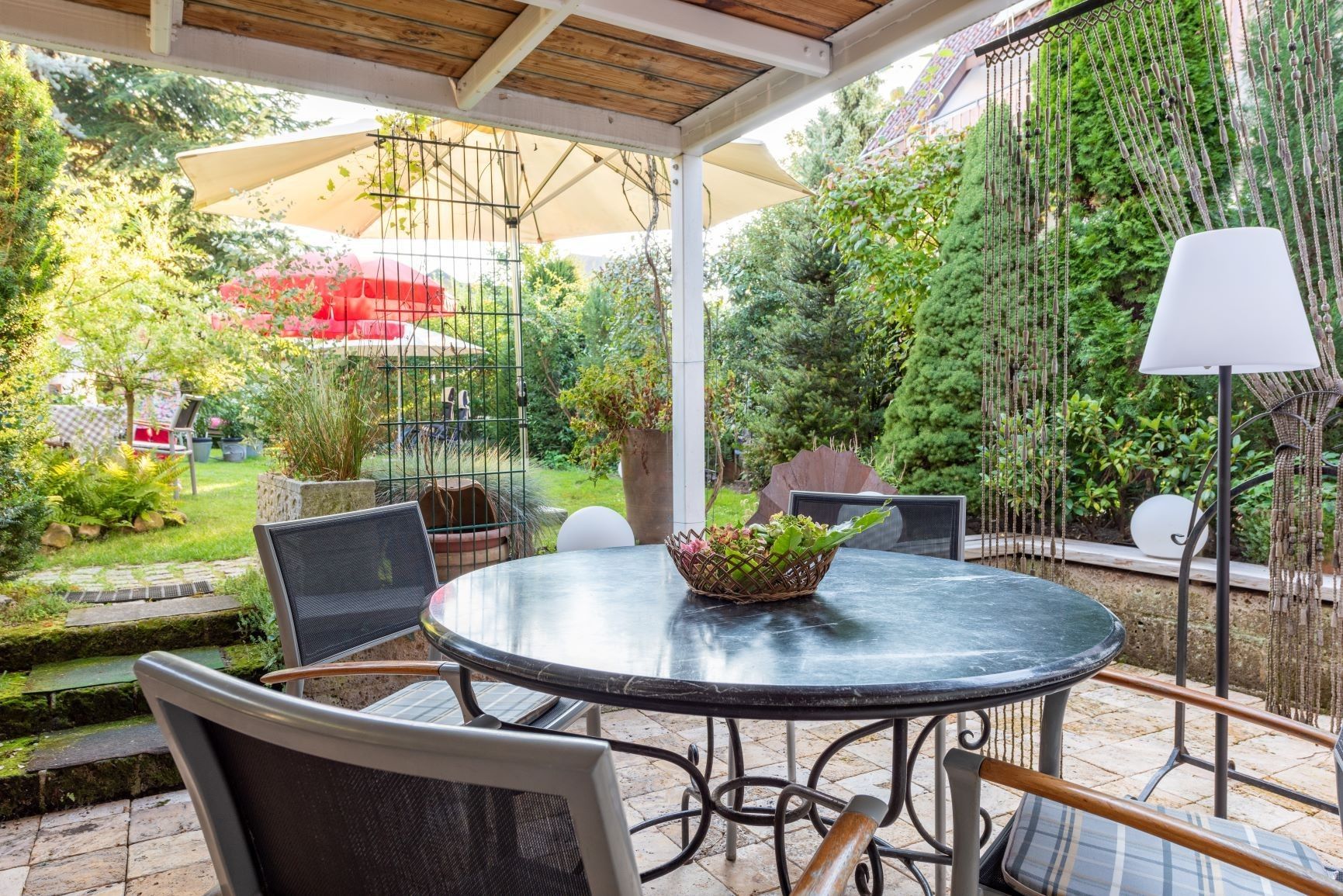 Eine Terrasse im Freien mit einem runden Tisch, Stühlen und einer Hängelampe.