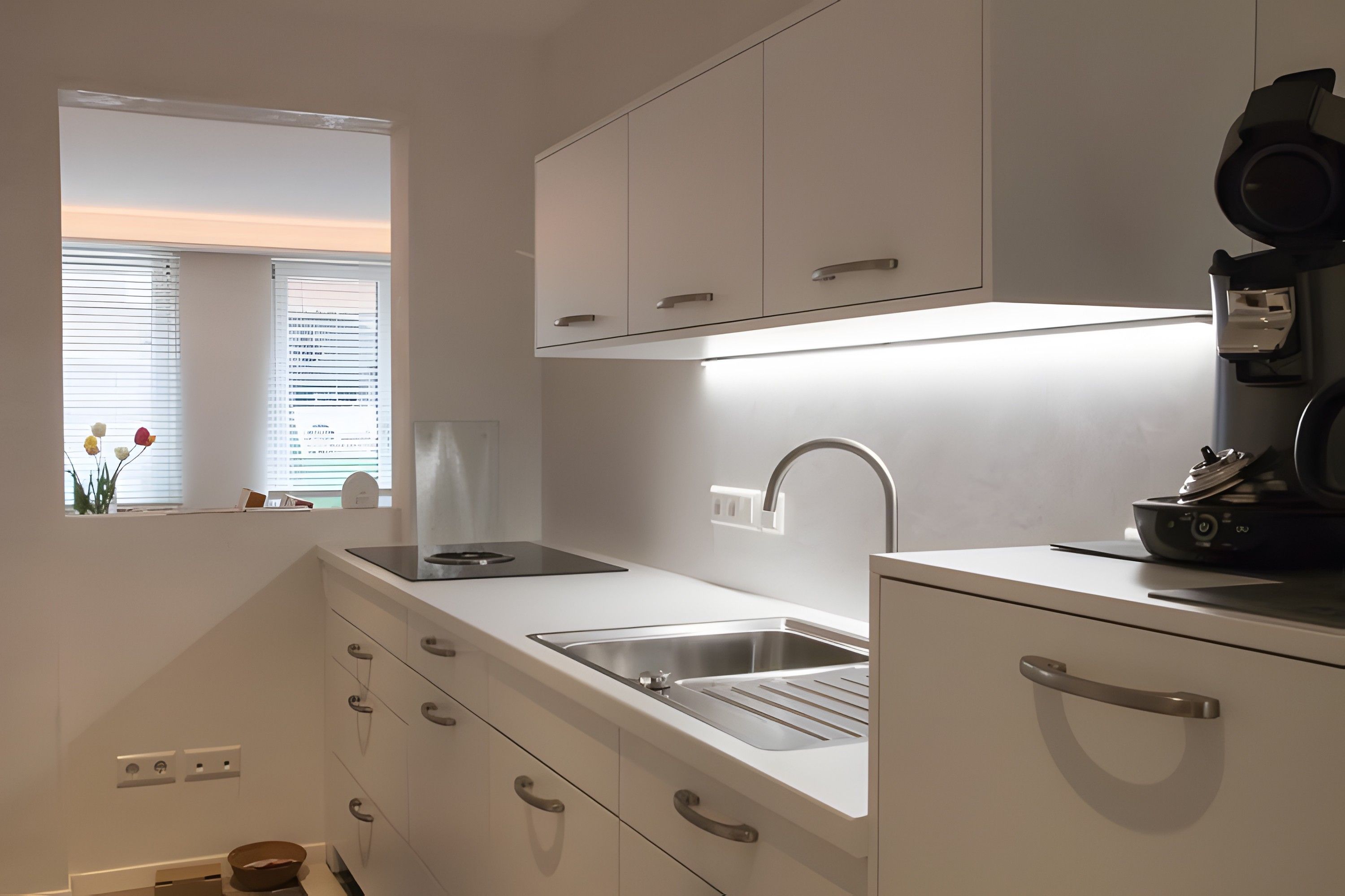 Een moderne keuken met een ingebouwde kookplaat, een roestvrijstalen spoelbak en witte keukenkastjes.