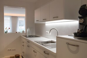 Une cuisine moderne dotée d’une cuisinière intégrée, d’un évier en acier inoxydable et de meubles de rangement blancs.