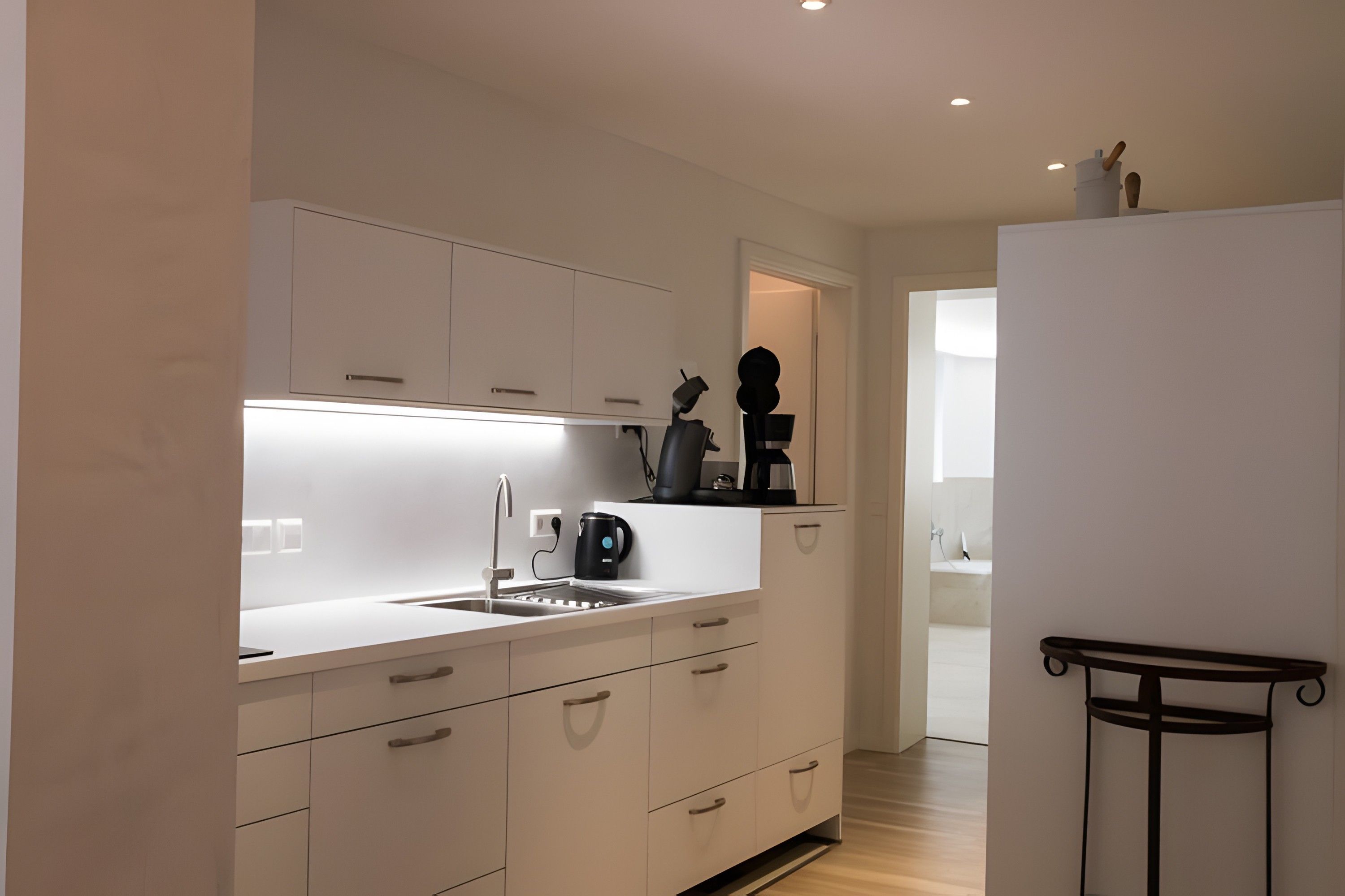 Una cocina moderna con armarios blancos, un lavamanos integrado y una cafetera.