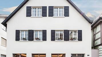 Ein zweistöckiges Gebäude mit einer symmetrischen Fassade, das einen zentralen Eingangsbereich mit einem überdachten Vorbau und zahlreiche Fenster mit Fensterläden aufweist.