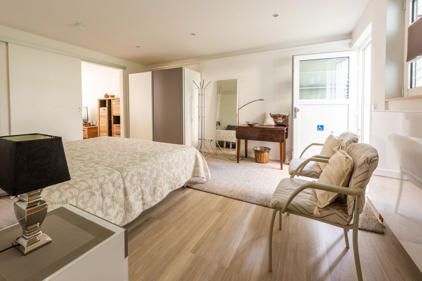 Un dormitorio con cama, mesita de noche, lámpara, silla y un escritorio con otra silla.