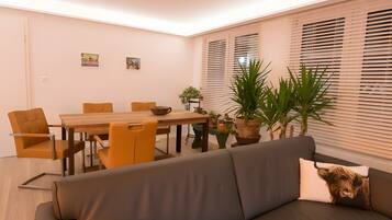Una sala de estar moderna con un sofá, mesa de comedor, sillas y plantas en macetas.