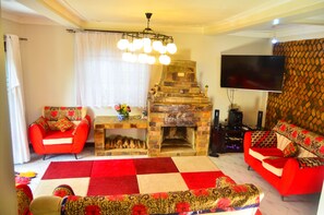 Una sala de estar con chimenea, sofás rojos, un televisor y un tapete estampado.