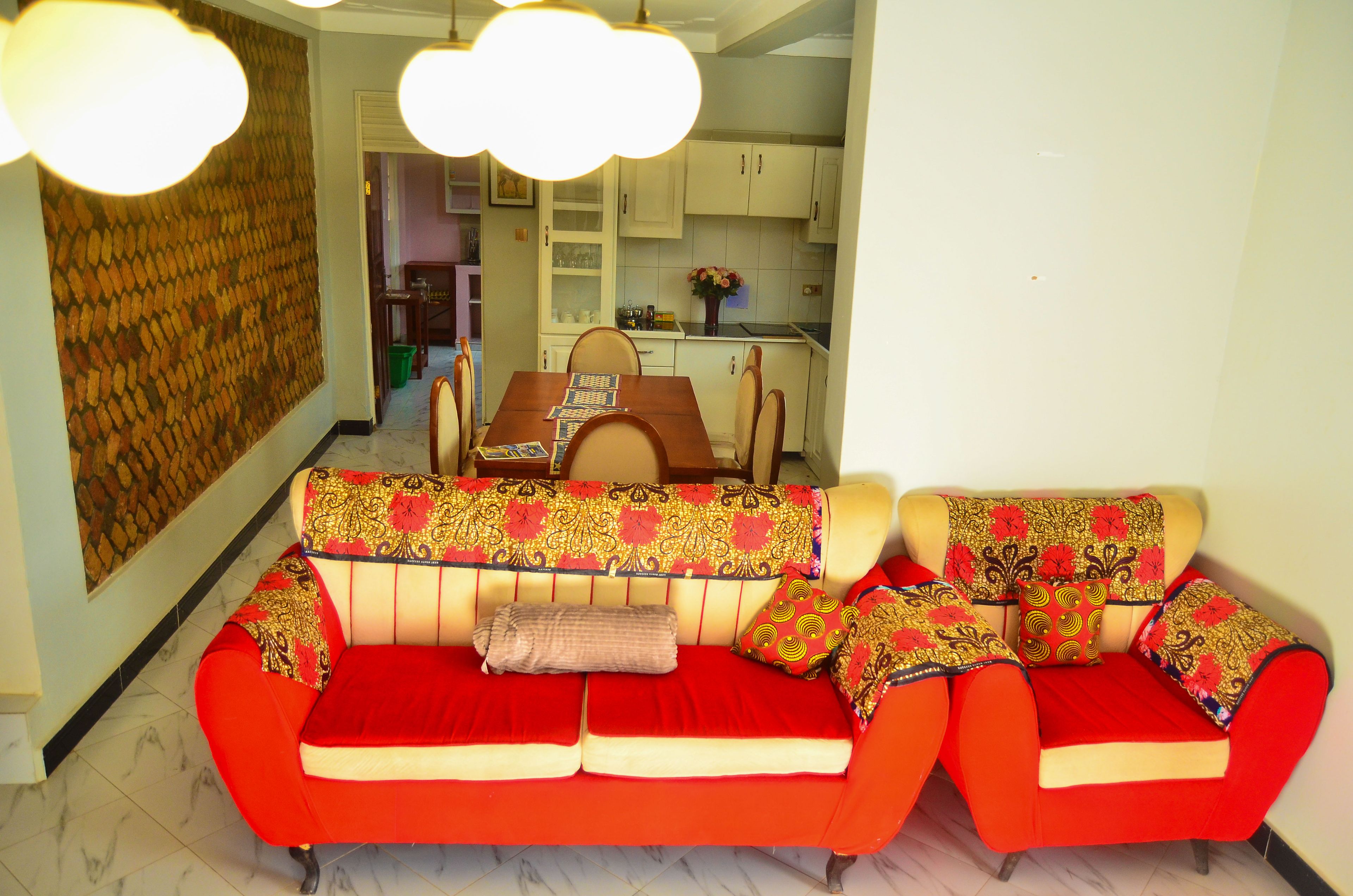 A living room with a red sofa set, a dining area with a wooden table, and a kitchen with white cabinets.