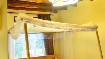 Una cama individual con dosel, cabecera de madera y colcha estampada con motivos florales.
