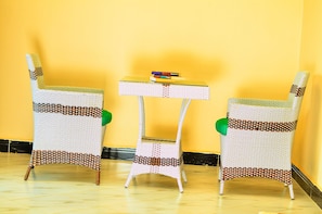 Three wicker chairs with a woven pattern, a small table with books, and a yellow wall.