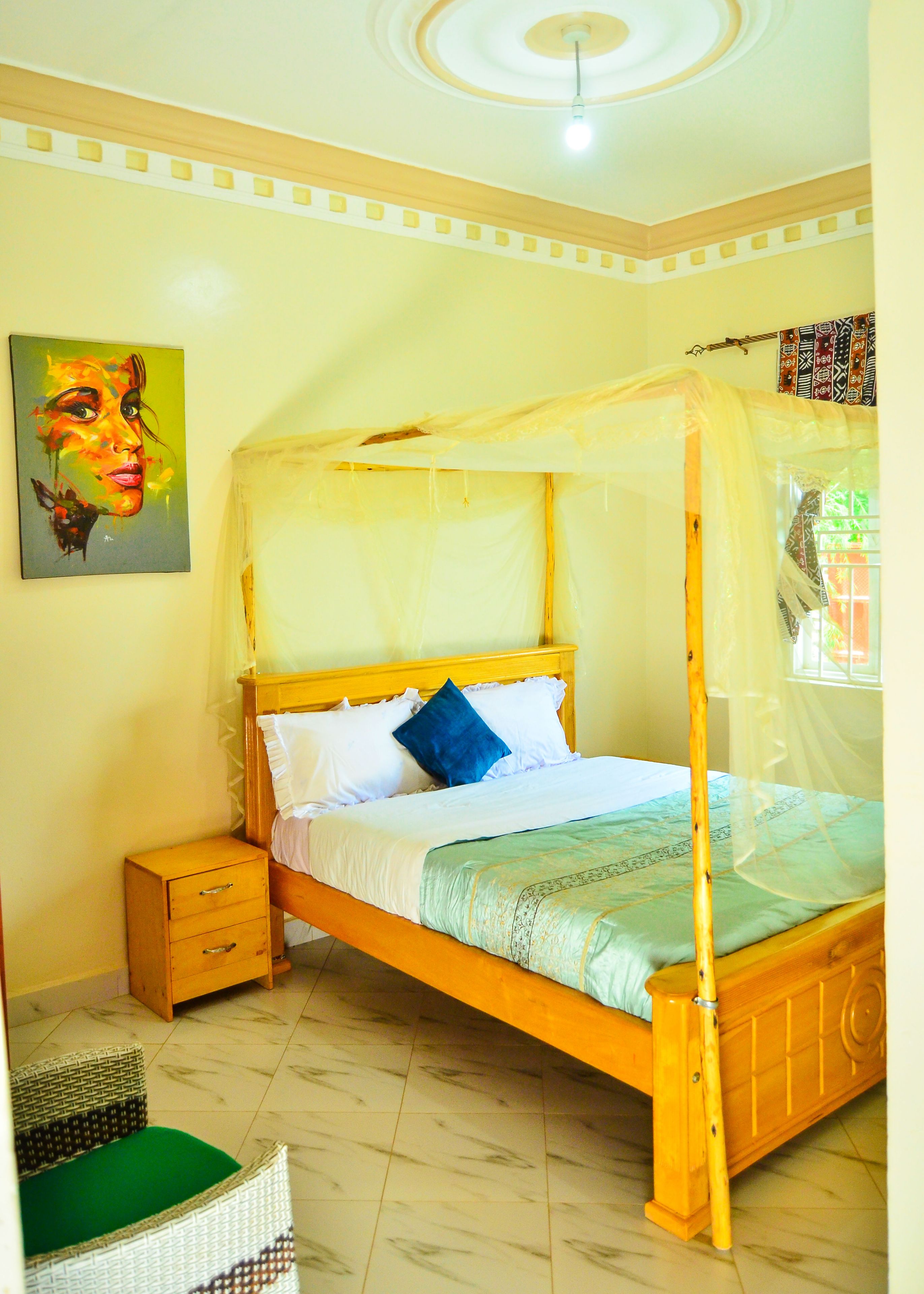 Een bed met hemelbed, een nachtkastje, een rieten stoel en een schilderij aan de muur.