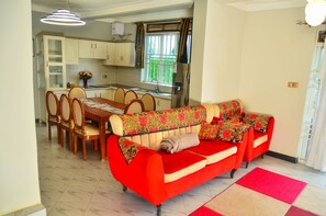 Un comedor con una mesa y sillas, una cocina con armarios y un refrigerador, y un sofá rojo con cojines estampados.