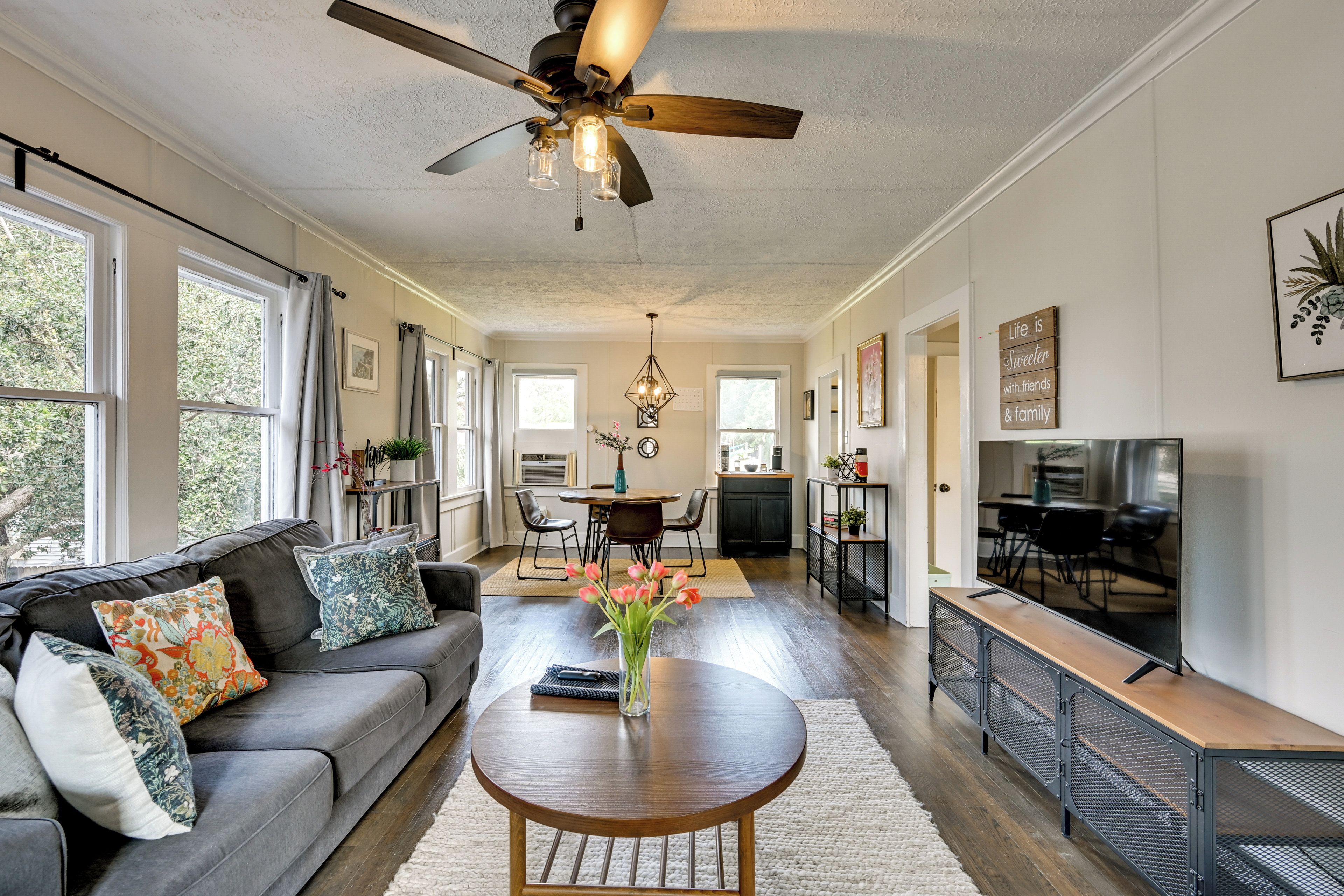 A spacious living room with a ceiling fan, a dining area with a table and chairs, and a kitchen area with a TV.