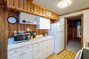 A kitchen with wooden paneling, a microwave, a refrigerator, and a clock. - Flip Flop Cottage: Lake Access in Clermont (Clermont)