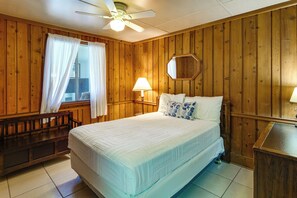 A bedroom with a bed, a nightstand, a lamp, a ceiling fan, and wooden walls. - Coconut Cottage: Community Amenities, Near Disney (Clermont)