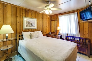 A wooden room with a bed, a ceiling fan, a framed picture, a nightstand, a lamp, and a TV. - Coconut Cottage: Community Amenities, Near Disney (Clermont)