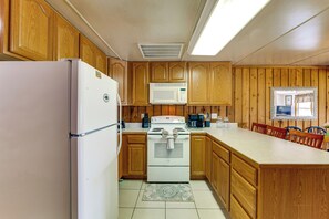 A kitchen with wooden cabinets, a white refrigerator, a microwave, a stove, and a dining area with a table and chairs. - Coconut Cottage: Community Amenities, Near Disney (Clermont)