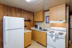 Eine kompakte Küche mit Holzausstattung, einem weißen Kühlschrank, einem Herd und einem Waschbecken.