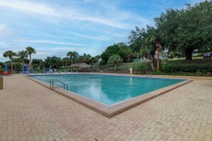 Ein rechteckiger Pool mit gefliestem Sonnendeck, umgeben von Palmen und einem überdachten Sitzbereich.
