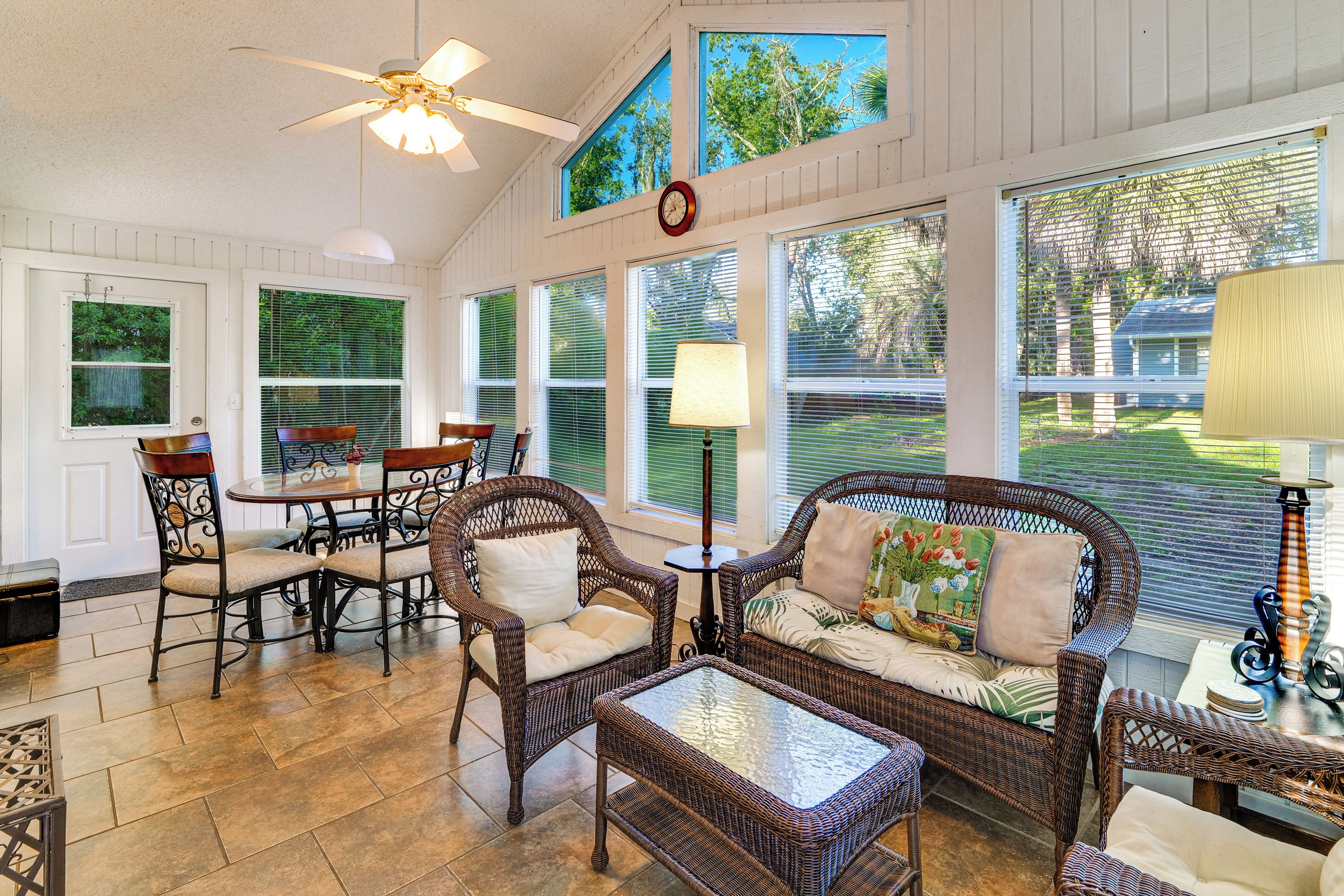 A sunroom with wicker furniture, large windows, and a ceiling fan.