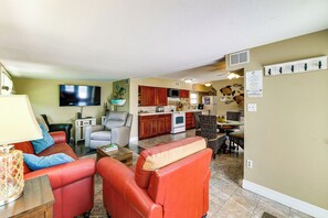 A living room with red leather sofas, a flat-screen TV, and a dining area with wicker chairs. - Sun-kissed Cottage: Lake Access, 14 Mi to Disney (Clermont)