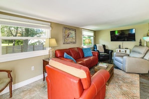 A living room with a red leather sofa, a beige armchair, a coffee table, and a television mounted on the wall. - Sun-kissed Cottage: Lake Access, 14 Mi to Disney (Clermont)