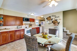 A kitchen with wooden cabinets, a microwave, a toaster, and a dining area with wicker chairs and a glass table. - Sun-kissed Cottage: Lake Access, 14 Mi to Disney (Clermont)