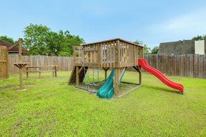 A wooden play structure with a slide and climbing area in a grassy backyard. - Game Room & Private Yard! Family Houston Escape (Houston)