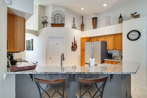 A kitchen with a central island, bar stools, a refrigerator, a coffee maker, and decorative items on the walls. - Spacious 4BR w/ South-facing Pool/spa: Disney 11mi (Clermont)