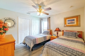 A bedroom with two beds, a ceiling fan, a bedside table with a lamp, a framed picture on the wall, and a mirror with a flower arrangement. - Spacious 4BR w/ South-facing Pool/spa: Disney 11mi (Clermont)