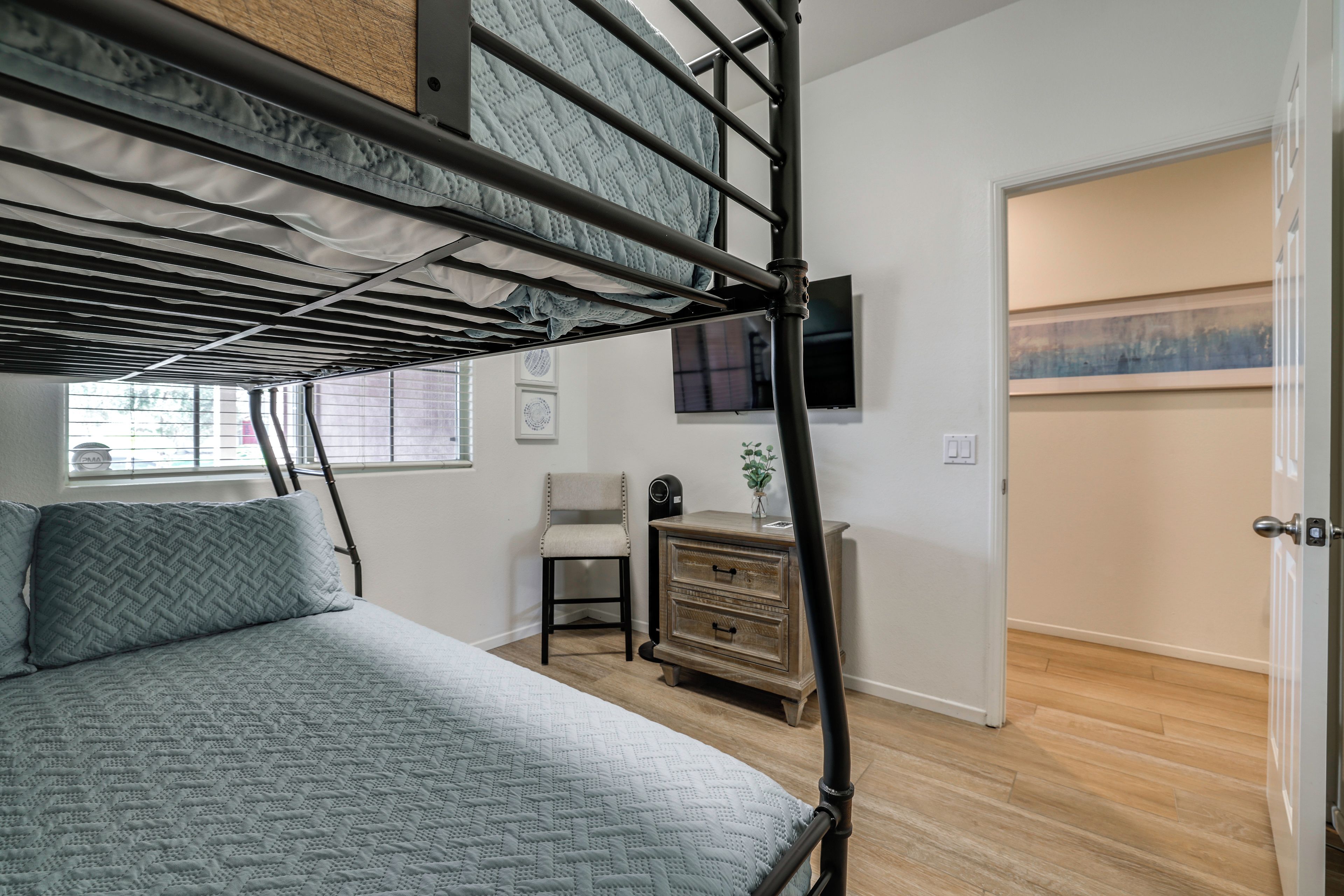 A bunk bed with a headboard, a bedside table, a chair, and a television on the wall.