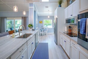 A modern kitchen with a central island, stainless steel appliances, and a dining area with a view of greenery outside. - 4 Minute Walk to Private Beach Plus a Private Pool (Vero Beach)