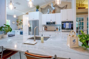 A modern kitchen with white cabinetry, a marble countertop, and a large island with a sink. - 4 Minute Walk to Private Beach Plus a Private Pool (Vero Beach)
