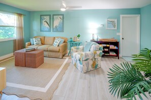 A living room with a sofa, armchair, and a small table with a lamp. There is a bookshelf with books and decorative items. - 4 Minute Walk to Private Beach Plus a Private Pool (Vero Beach)