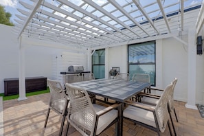 Un patio exterior con una pérgola, una parrilla y una mesa con sillas.