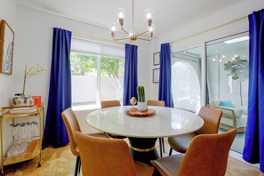 Uma sala de jantar com mesa redonda, cadeiras, lustre e cortinas azuis.