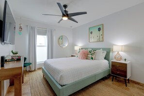 A bedroom with a bed, a desk, a chair, a ceiling fan, a window with curtains, a wall-mounted mirror, and a bedside table with a lamp. - Walk to Wigwam Resort! Family & Golfers Oasis (Litchfield Park)