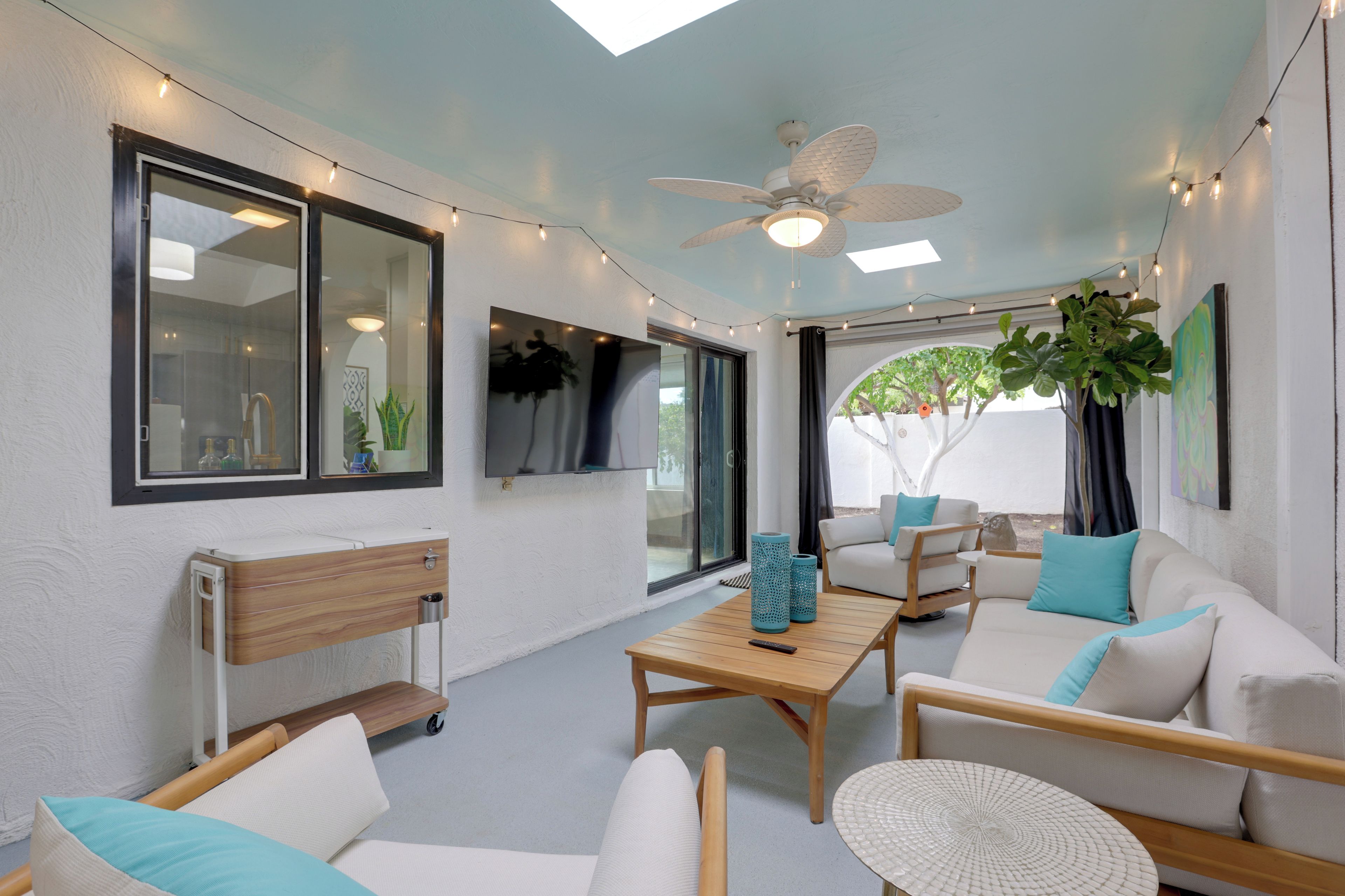 Uma sala de estar moderna com ventilador de teto, TV fixada na parede e uma grande janela que oferece vista para o exterior.