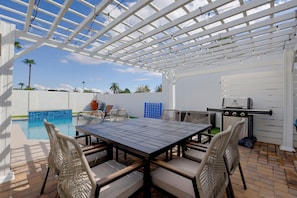 Um alpendre coberto com piscina, móveis de exterior e churrasqueira.