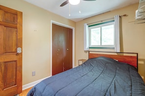 Ein Schlafzimmer mit einem Bett, einer Holztür, einem Fenster mit Vorhängen und einem Deckenventilator.