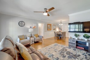 Ein modernes Wohnzimmer mit einer Couch, einem Couchtisch, einem Essbereich mit Stühlen, einem Fernseher und einem Deckenventilator.