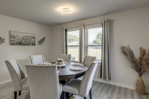 A dining area with a round table, six chairs, and a vase with dried plants. - The Geaux House - 1 Mi to Tiger Stadium (Baton Rouge)