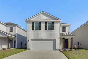 A two-story residential building with a central garage door, a front entrance with a door, and a small porch area. - The Geaux House - 1 Mi to Tiger Stadium (Baton Rouge)