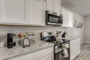 A modern kitchen with white cabinetry, a stainless steel microwave, a stove, and a coffee station. - The Geaux House - 1 Mi to Tiger Stadium (Baton Rouge)