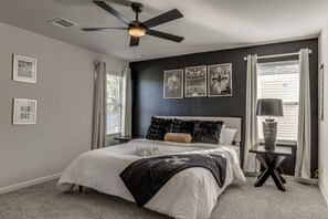 A bedroom with a bed, a ceiling fan, a nightstand, a lamp, and framed pictures on the wall. - The Geaux House - 1 Mi to Tiger Stadium (Baton Rouge)