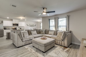 A modern living room with a sectional sofa, a coffee table, and a dining area with a kitchen in the background. - The Geaux House - 1 Mi to Tiger Stadium (Baton Rouge)