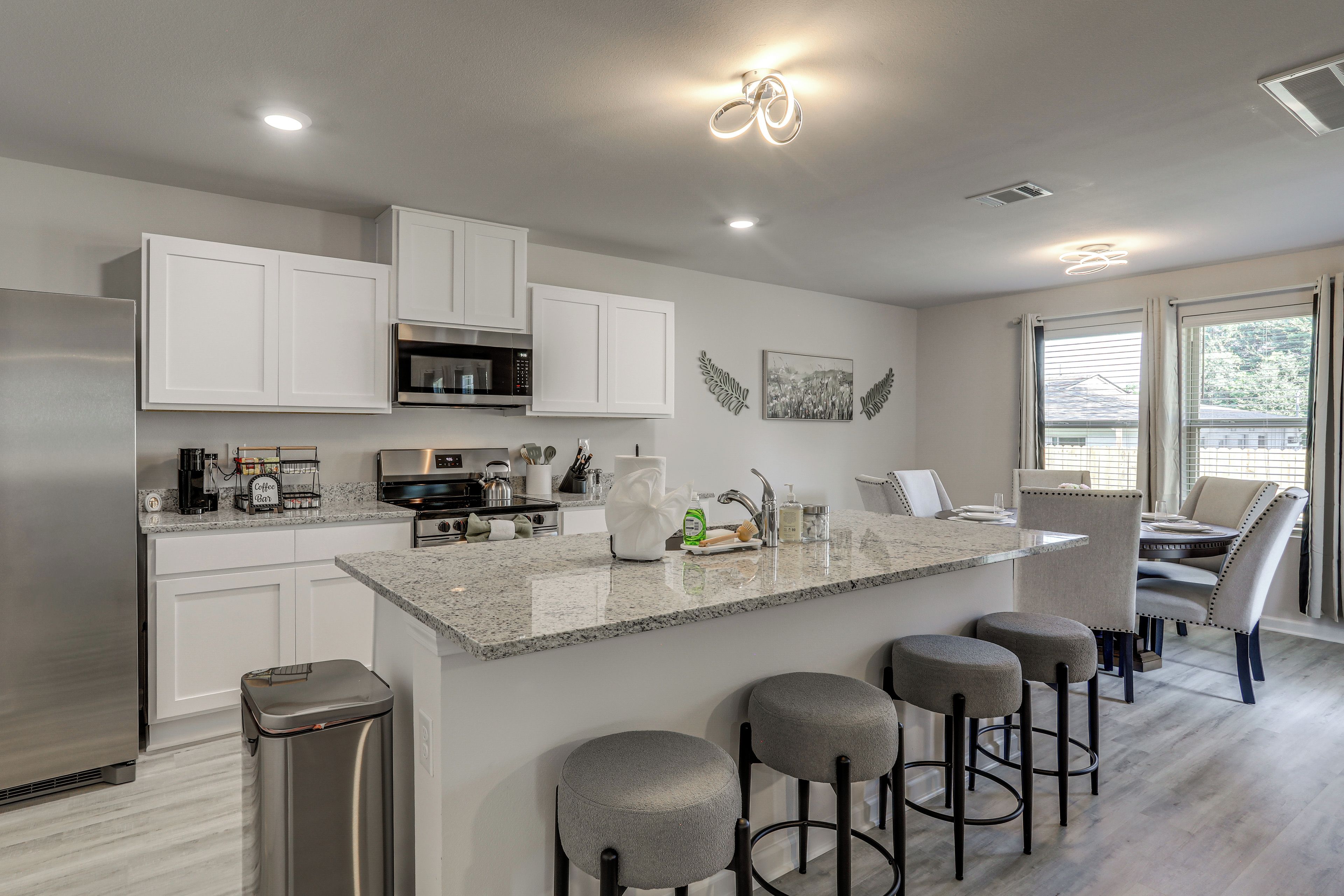 A modern kitchen with white cabinetry, a stainless steel range, and a bar area with stools.