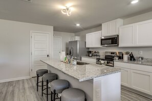A modern kitchen with a central island, bar stools, stainless steel appliances, and white cabinetry. - The Geaux House - 1 Mi to Tiger Stadium (Baton Rouge)